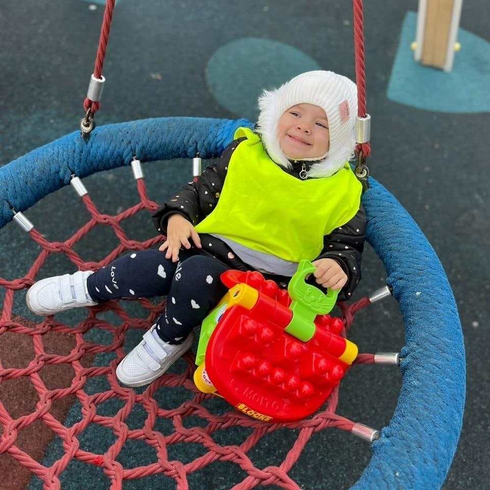 Малыш качается на безопасной качели под присмотром воспитательницы Малыш качается на безопасной качели под присмотром воспитательницы