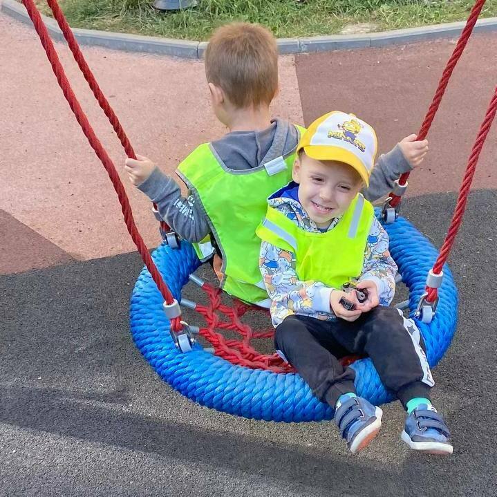 Дети качаются на качели во время прогулки у садика Дети качаются на качели во время прогулки у садика